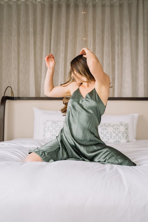 Woman in Green Sleeveless Dress Sitting on the Bed