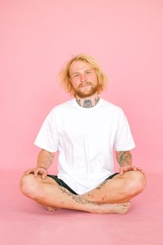 一个穿着休闲装的年轻人坐在粉色背景前，微笑着看向镜头
