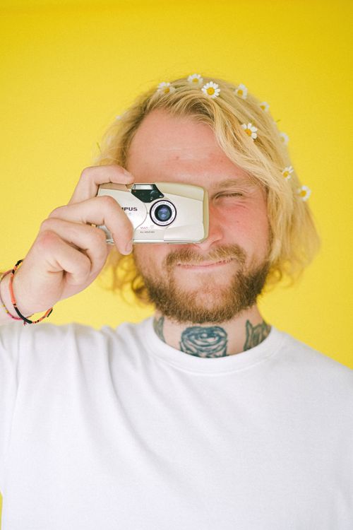 Free Young male in casual outfit and with blond hair taking photo with camera while standing on yellow background Stock Photo