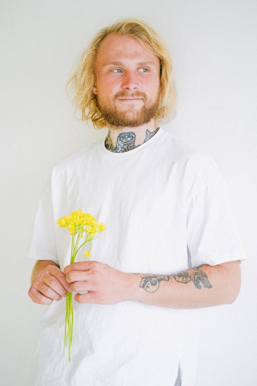 Free Contemplative adult unshaven male with tattoos and colorful blossoming flower bouquet looking away on white background Stock Photo