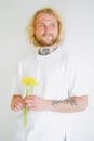 Contemplative adult unshaven male with tattoos and colorful blossoming flower bouquet looking away on white background