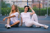 锻炼后，年轻的金发女运动员盘腿坐在城里穿着运动服的女伴旁边