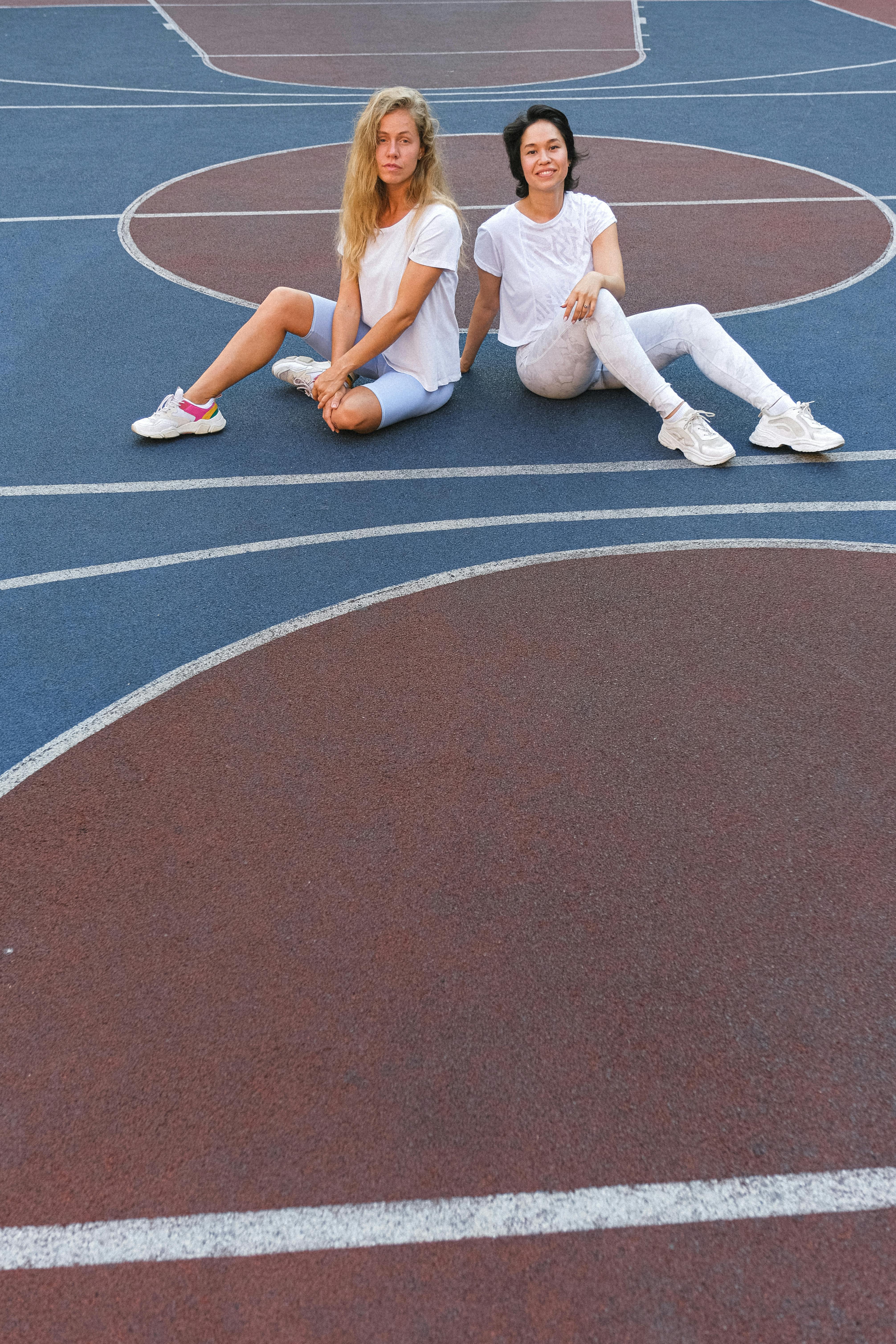 young female friends resting on floor in sport court