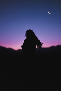 黄昏时分，一位长发女子的剪影映衬在星空和新月之下