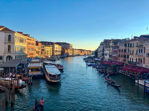 Free Explore a vibrant sunset view of Venice's historic Grand Canal lined with colorful buildings and gondolas. Stock Photo
