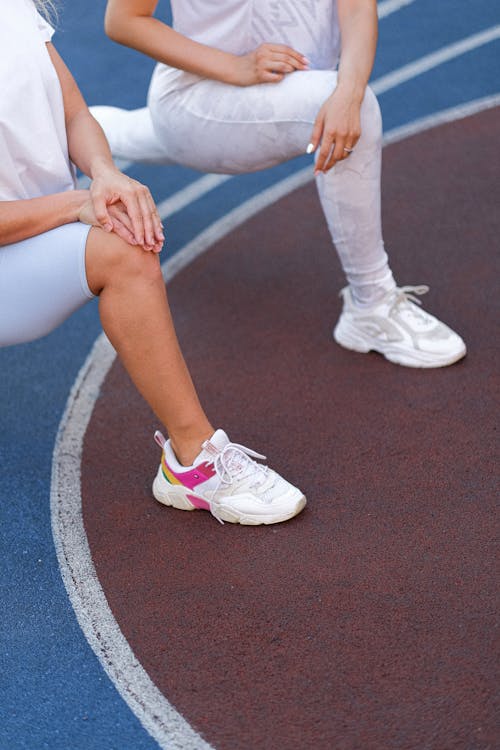 Free High angle of unrecognizable women in sportswear stretching legs before training on stadium Stock Photo