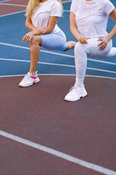 Two women doing lunges on an outdoor track, showcasing activewear and fitness lifestyle.
