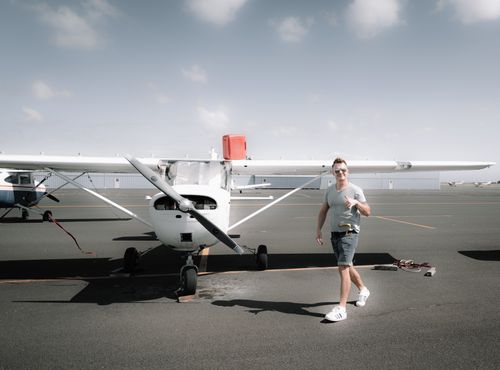Free Full body young happy male wearing casual clothes strolling near modern propeller jet parked on airfield on clear summer day and showing thumb up Stock Photo