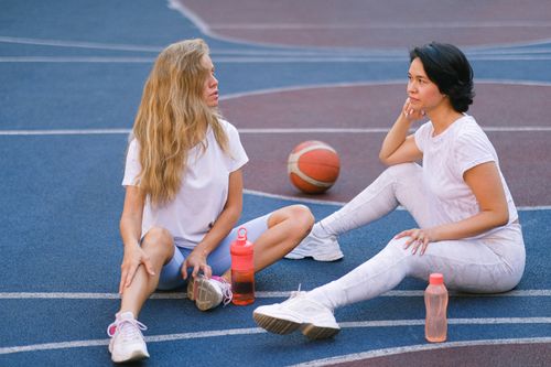 Free Full length of confident young ladies in sportswear speaking while having break on court after exercising with water bottles near basketball in daylight Stock Photo