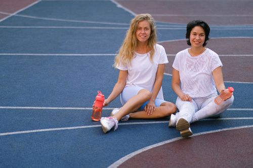 Free Full length of smiling young women in sportswear having break on basketball court after training with water bottles and looking at camera in daylight Stock Photo