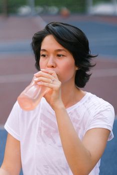 白天，一位穿着运动服的年轻女子在运动场上喝水，目光移开