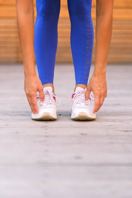 Crop unrecognizable sportswoman stretching and bending down in gym