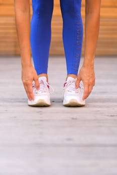 A woman exercising, touching toes in bright blue leggings and sneakers indoors.
