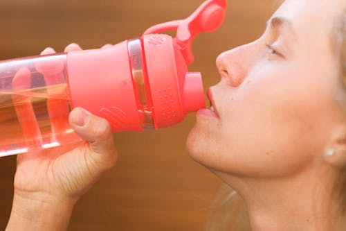 Free Side view crop pretty thirsty female drinking fresh cold water from reusable bottle outside cottage Stock Photo