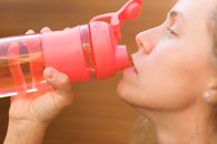 Side view crop pretty thirsty female drinking fresh cold water from reusable bottle outside cottage