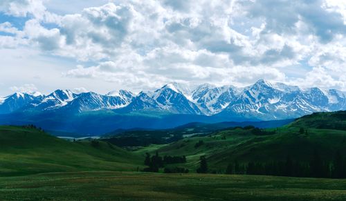 Free Stunning snow-capped mountain range surrounded by lush green valleys under cloudy skies. Stock Photo