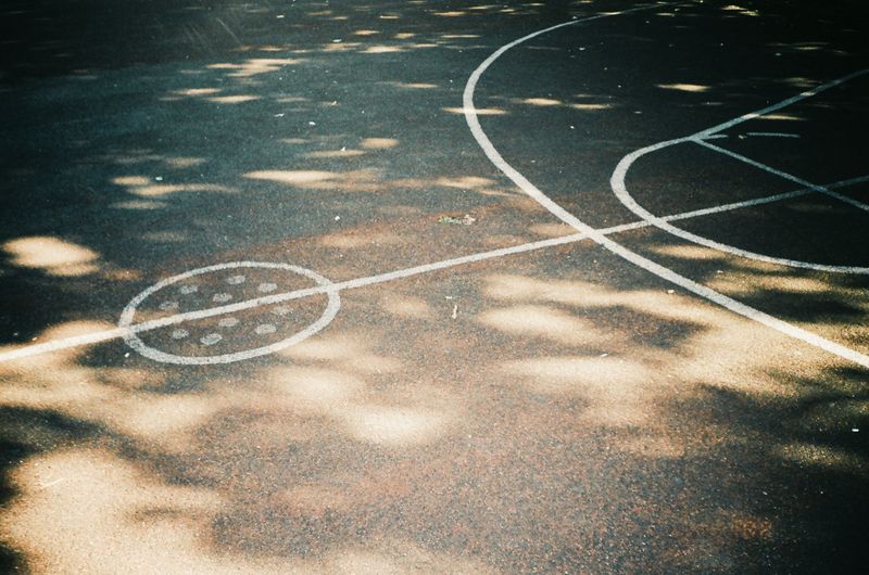 An empty outdoor basketball court with sunlight falling across the painted lines — photo by Inga Seliverstova on Pexels
