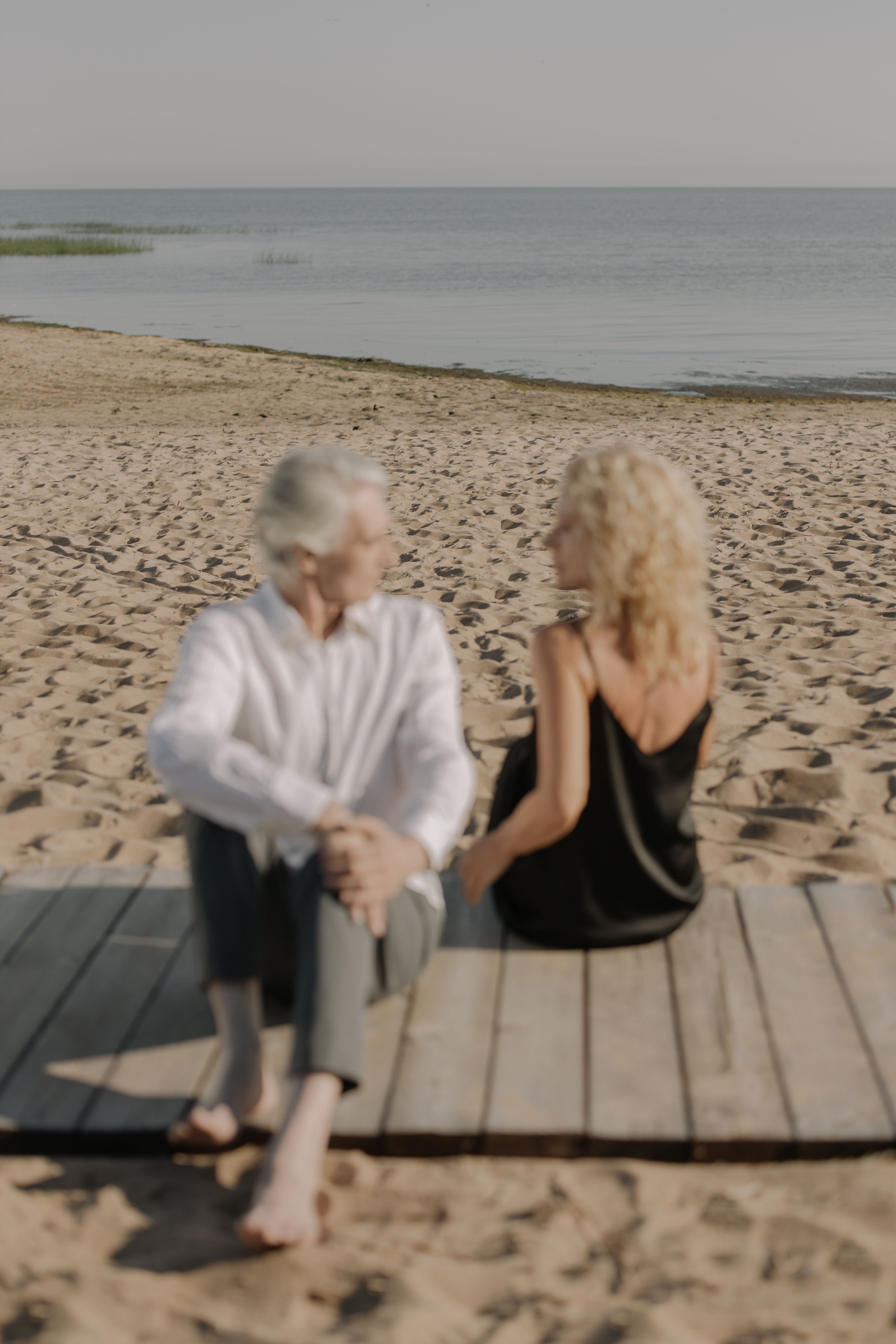Senior couple sitting on a wooden dock by the sea, enjoying a peaceful moment.