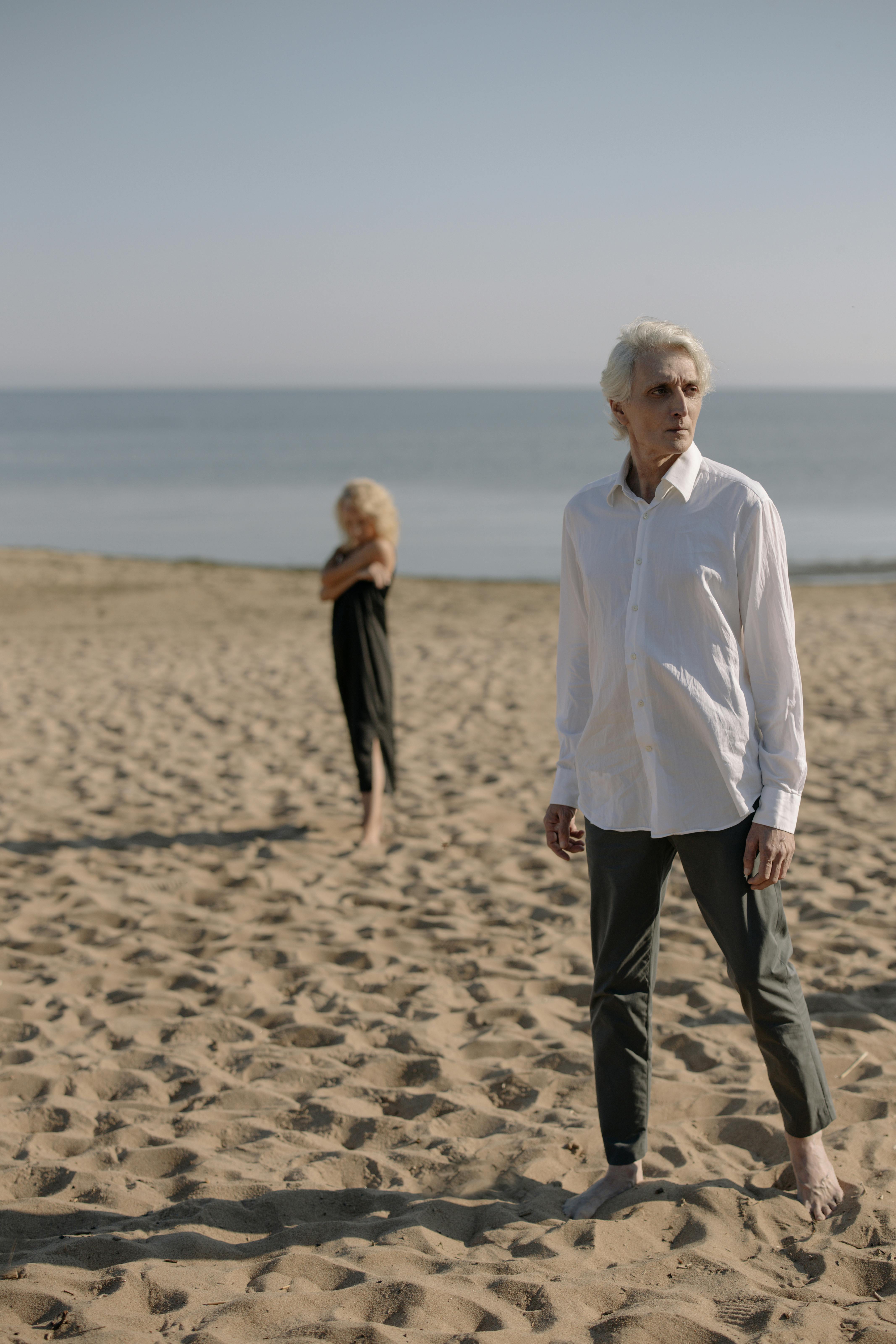 Elderly couple standing on a tranquil sandy beach, conveying a peaceful and reflective mood.