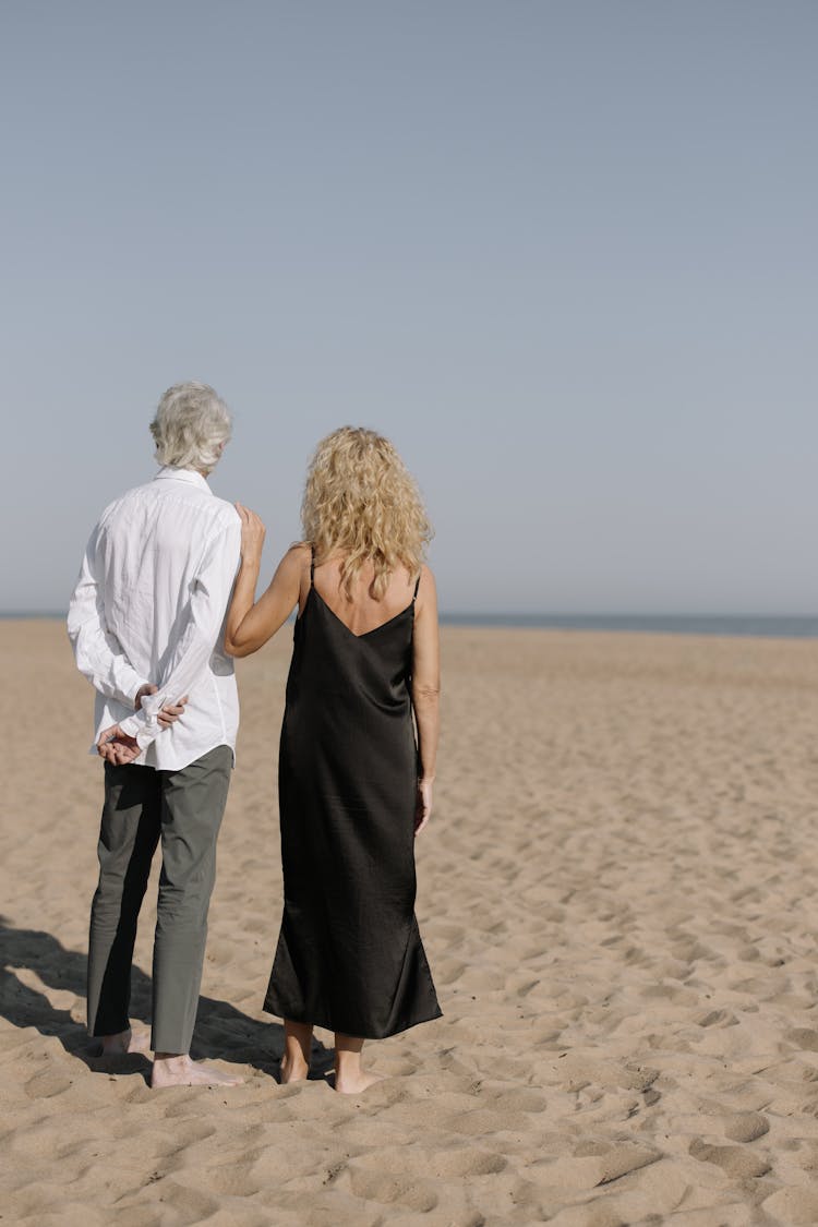 Back View Of Elderly Couple Standing On Brown Sand 