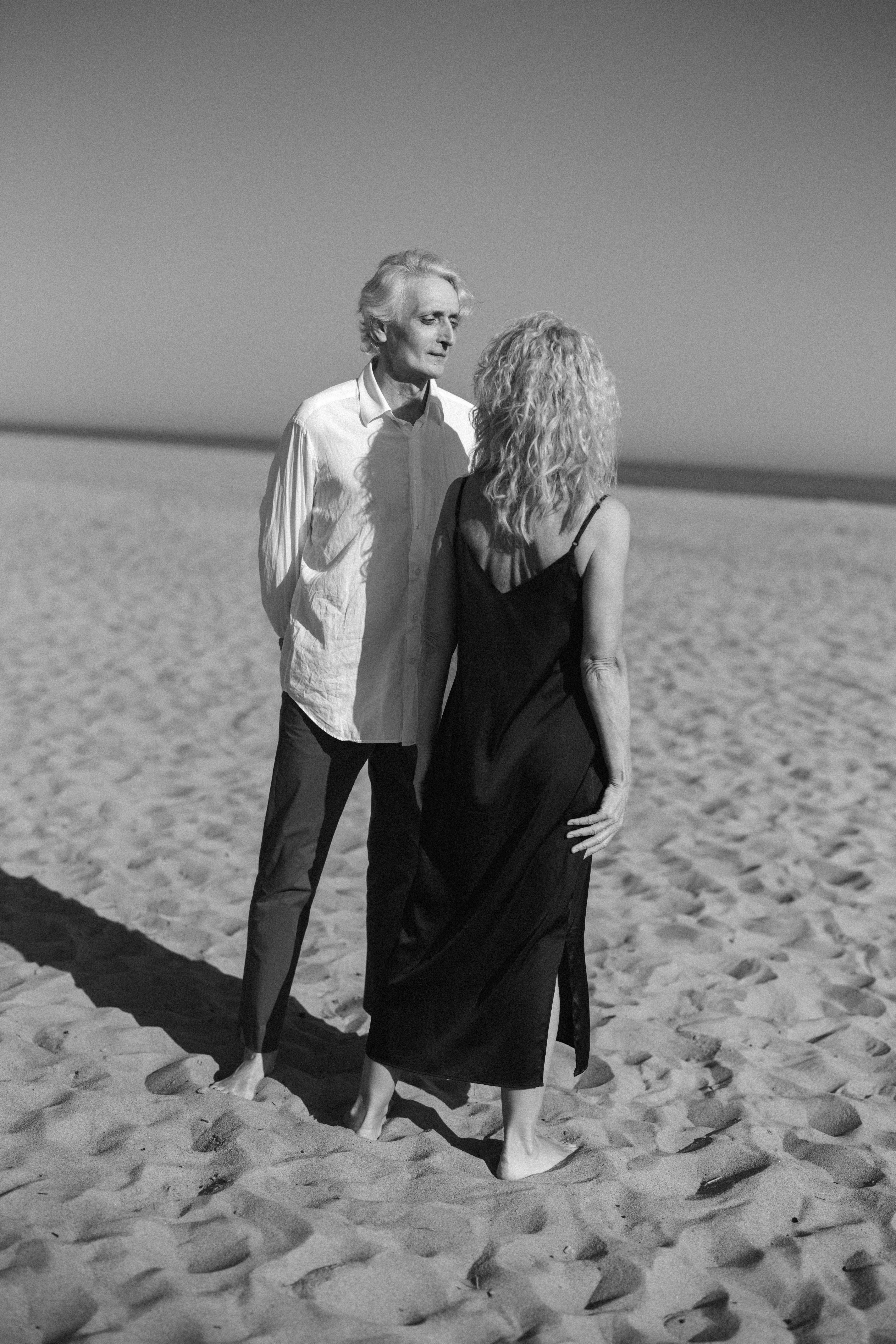 Couple walking on a sandy beach in a black and white photograph, evoking romance.