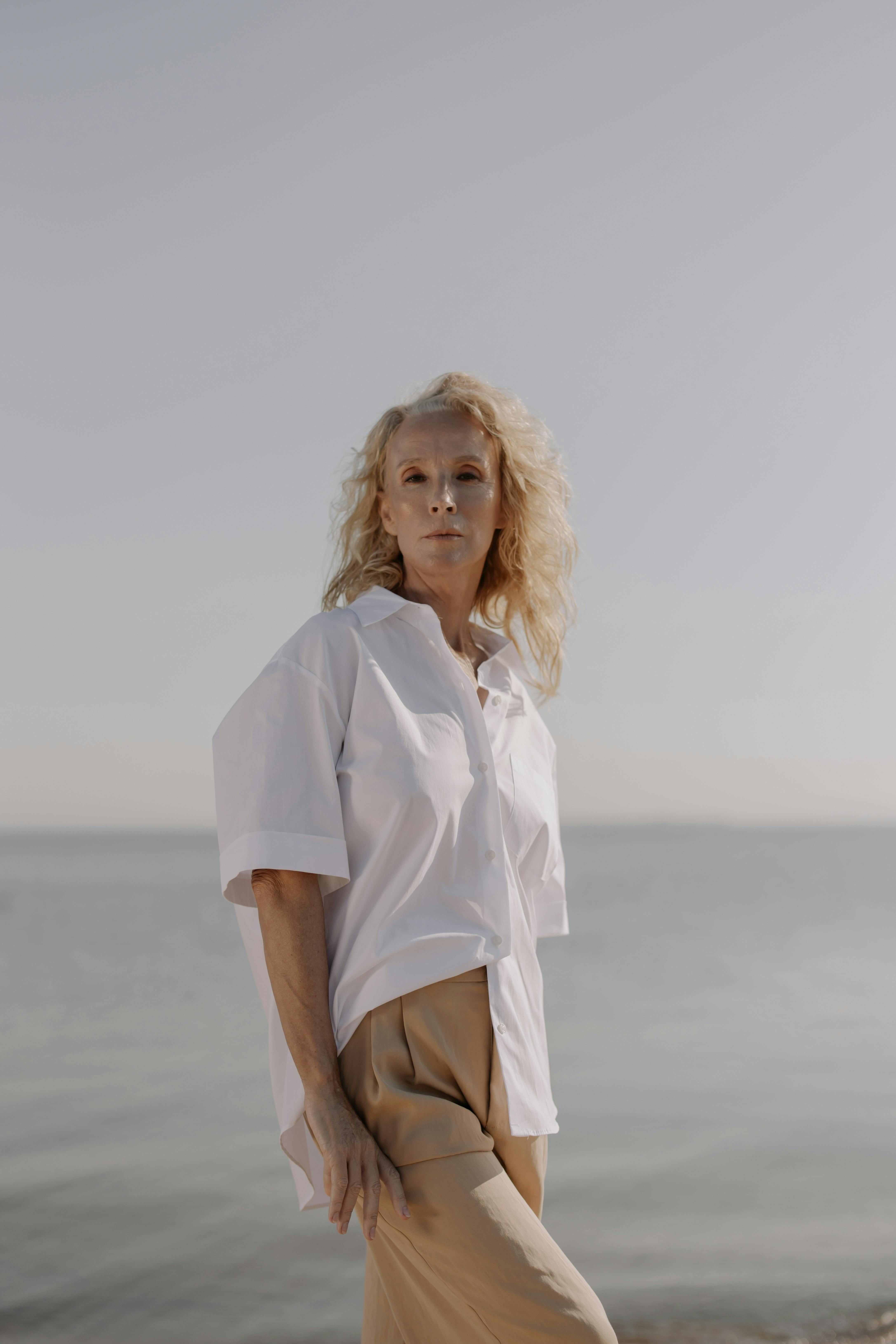 日落时分，一位穿着白衬衫的时尚高级女士在海边优雅地摆姿势