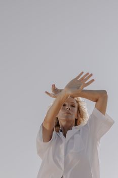 一位金发女子身穿白衬衫，在晴朗的天空下优雅地摆出姿势，尽显美丽与优雅