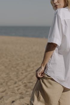 一名女子身穿白衬衫和米色裤子，站在沙滩上，轻松捕捉夏日氛围