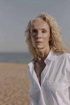 一位金发时尚的资深女性在阳光明媚的海滩上优雅地摆着姿势
