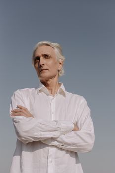 一名年长男子穿着白衬衫，在晴朗的白天户外自信地摆出姿势