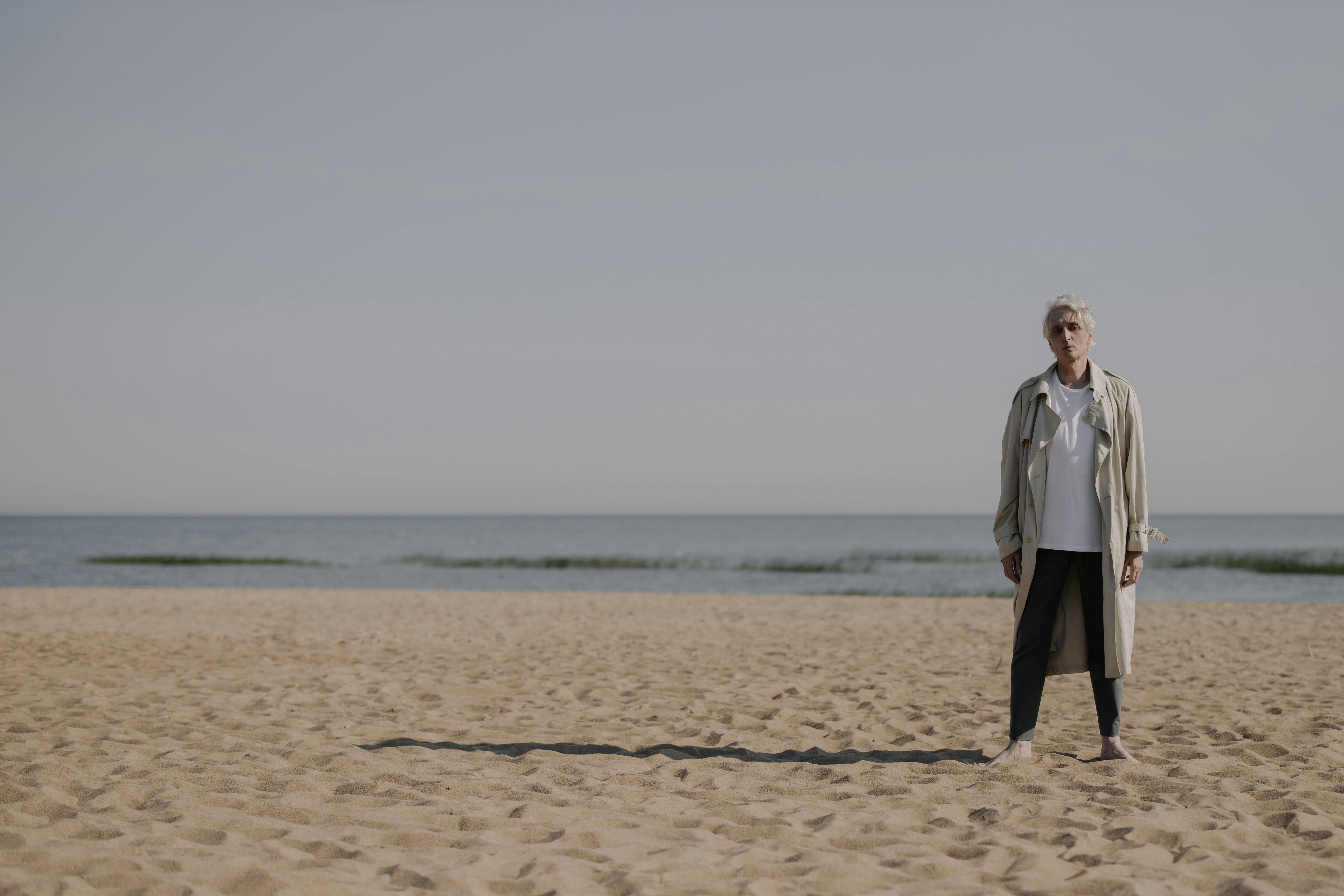 woman in gray coat standing on brown sand