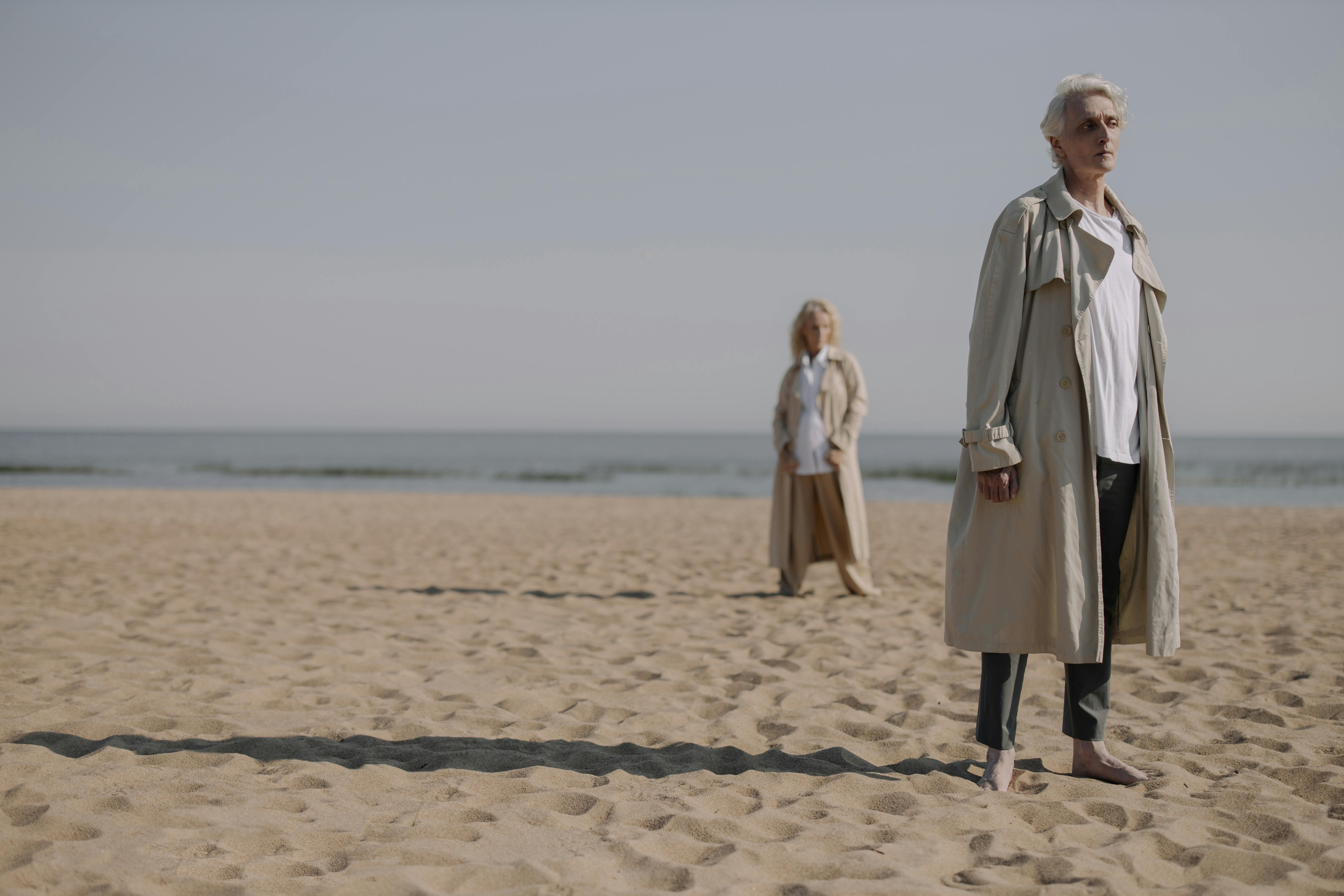 man in gray coat standing on brown sand