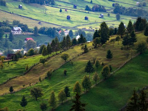 Free Serene countryside landscape in Romania with lush green hills and scattered houses in summer. Stock Photo