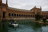 People Riding on Blue and White Boat on River Near Brown Concrete Building