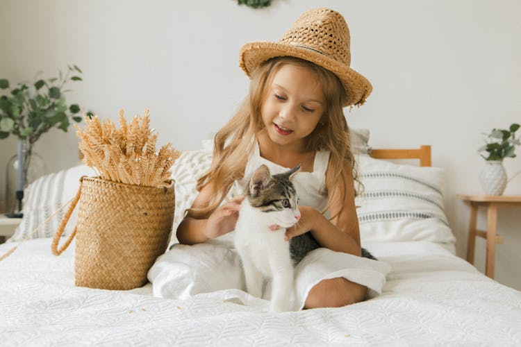 Happy Girl Sitting On Bed Playing With Cat