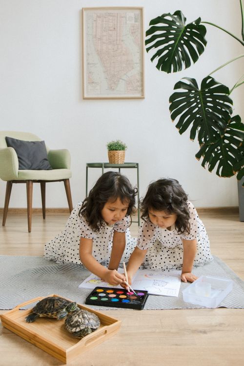 Free Two young sisters enjoying a painting session at home with turtles on a tray nearby. Stock Photo