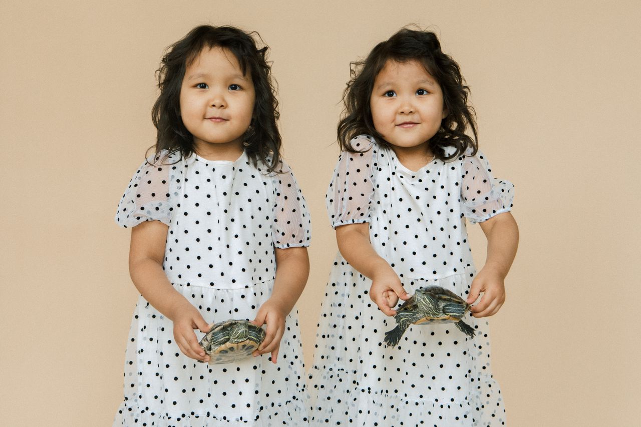 adorable twin girls in polka dot dresses happily holding turtles in a