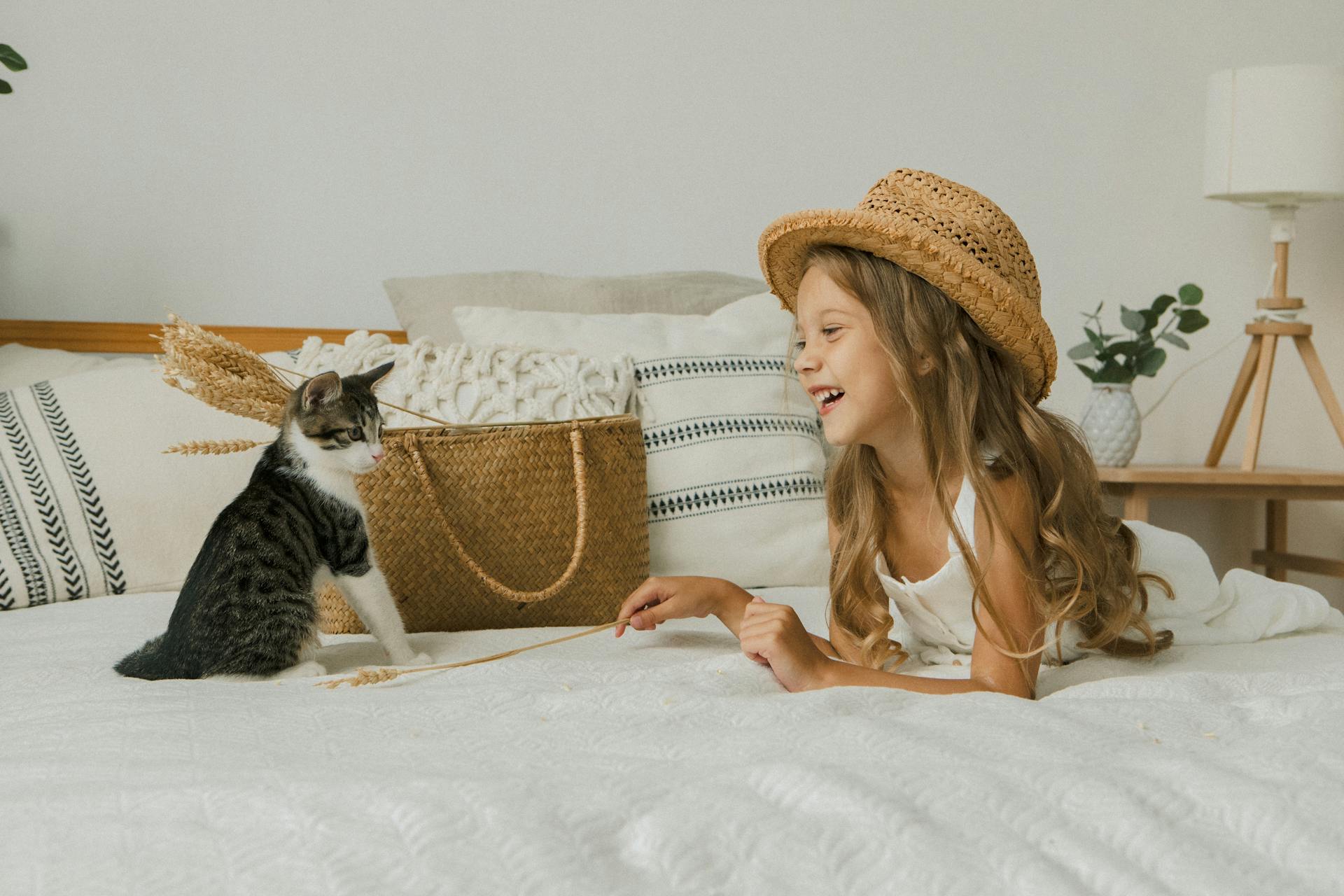 Photo of a Cat and Girl in a Hat Lying on Bed
