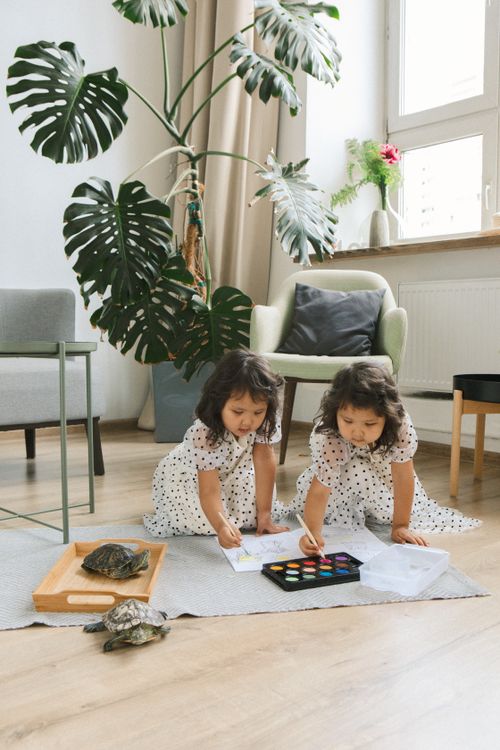 Free Twin girls painting with watercolors indoors surrounded by plants and pet turtles. Stock Photo