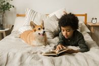 Boy in Gray Jacket Lying on Bed With Brown and White Dog