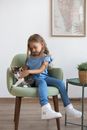Little Girl Sitting in an Armchair Petting a Cat 