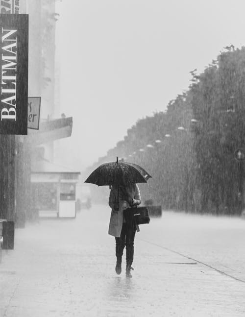 Free Grayscale Photo of a Person Holding an Umbrella while Walking on the Street Stock Photo