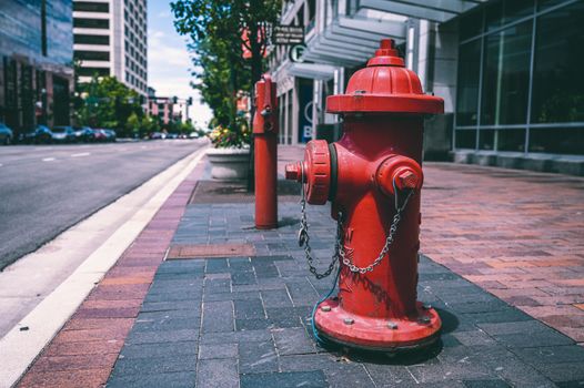 Red fire hydrant with chains located on empty street near road and building on sunny day