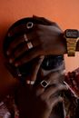 Anonymous African American man with stylish rings and golden wristwatch covering face with hands