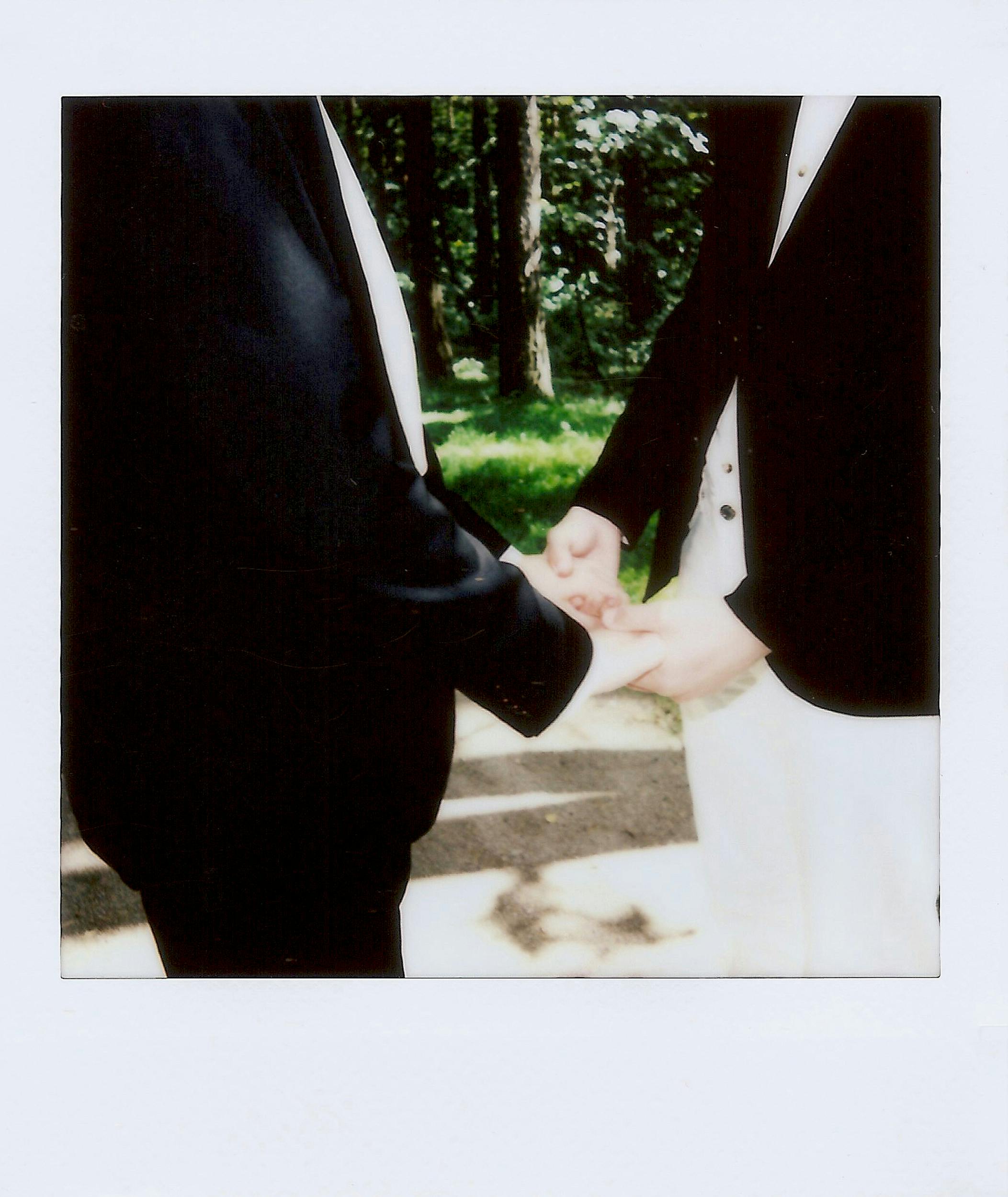 A romantic scene of a same-sex couple holding hands outdoors at their wedding day.