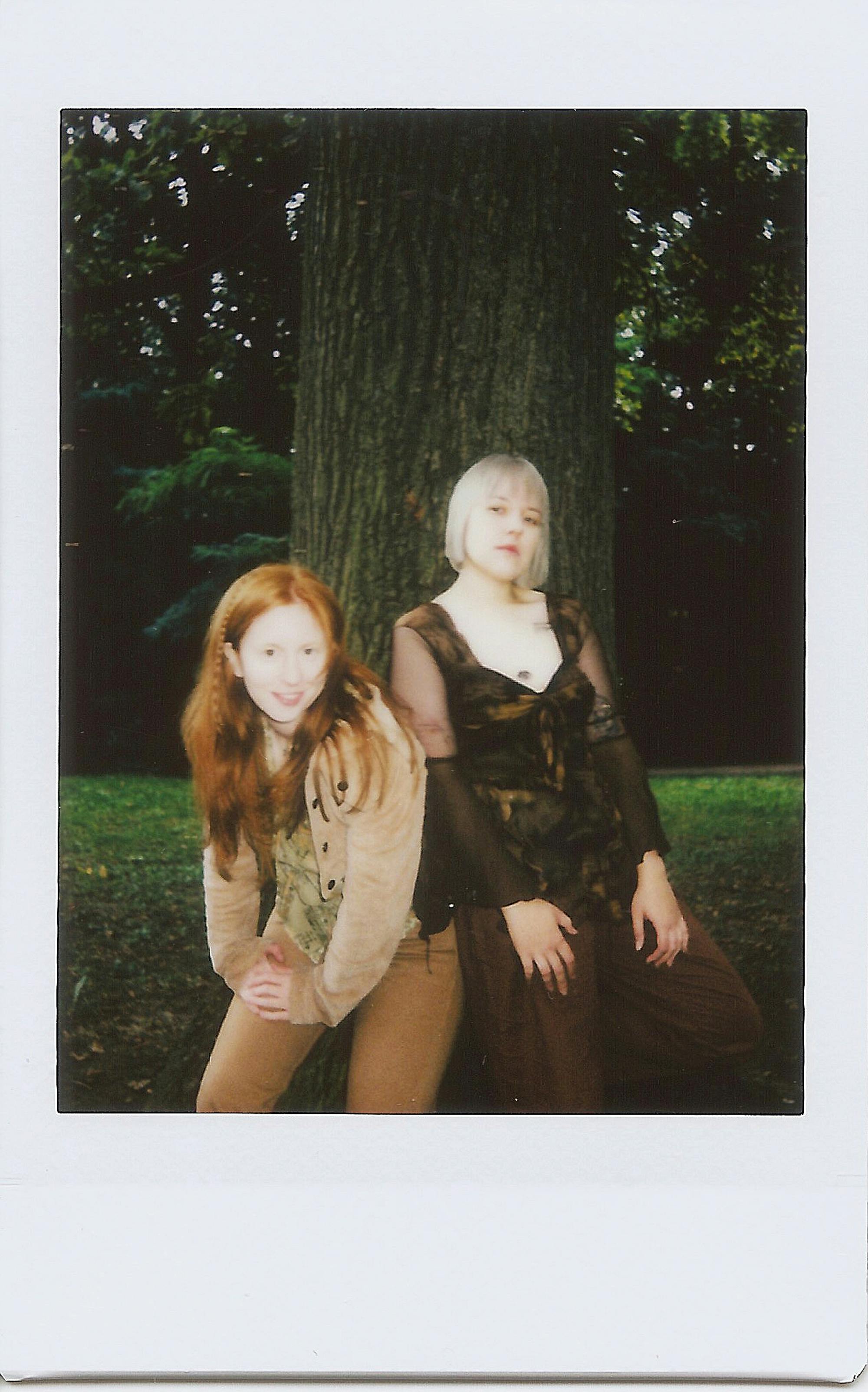 这是一张怀旧的即时照片，照片中两名女子在一棵绿树旁摆姿势，周围环境郁郁葱葱