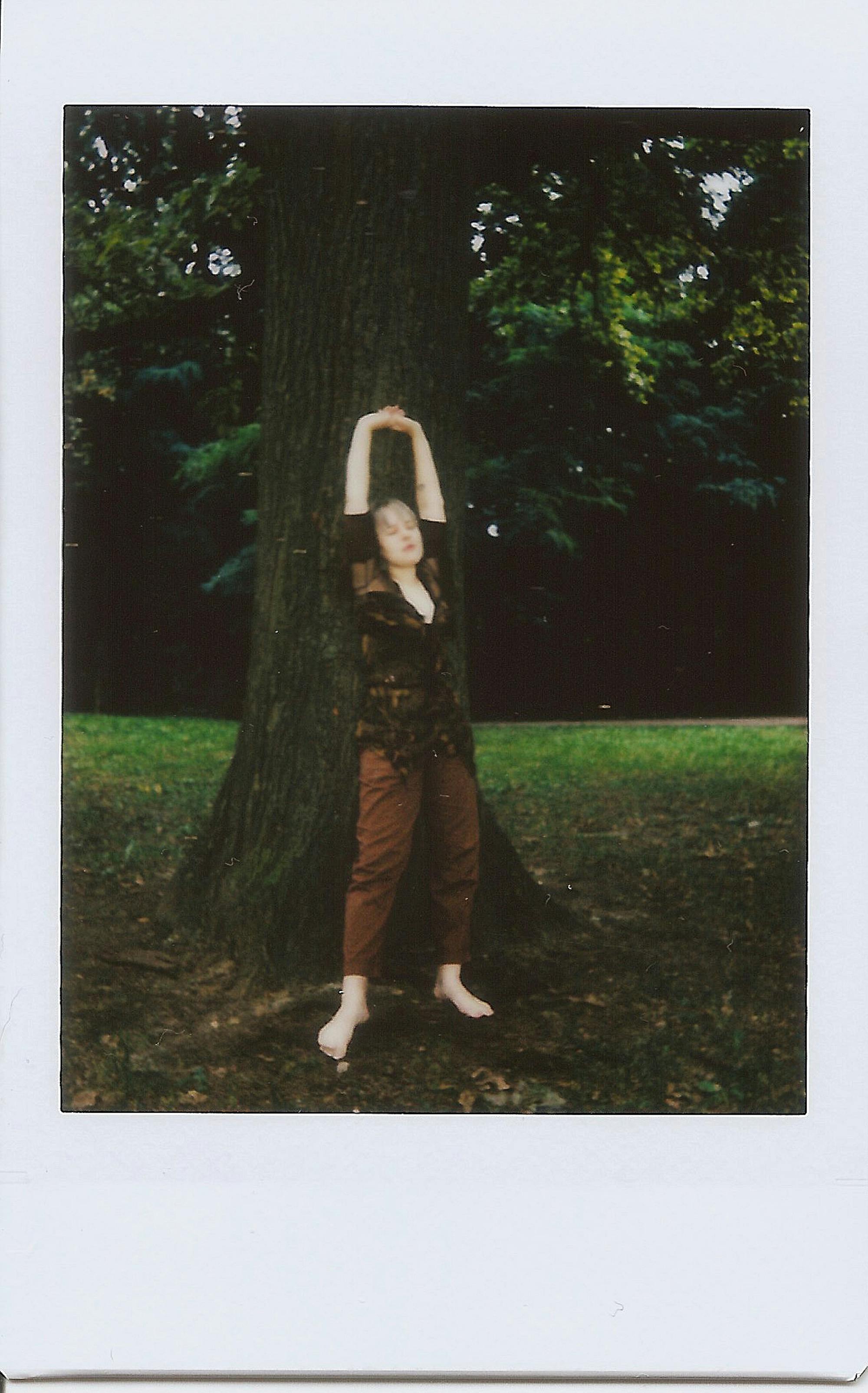 A woman stretches outdoors leaning against a large tree, captured in a vintage style.