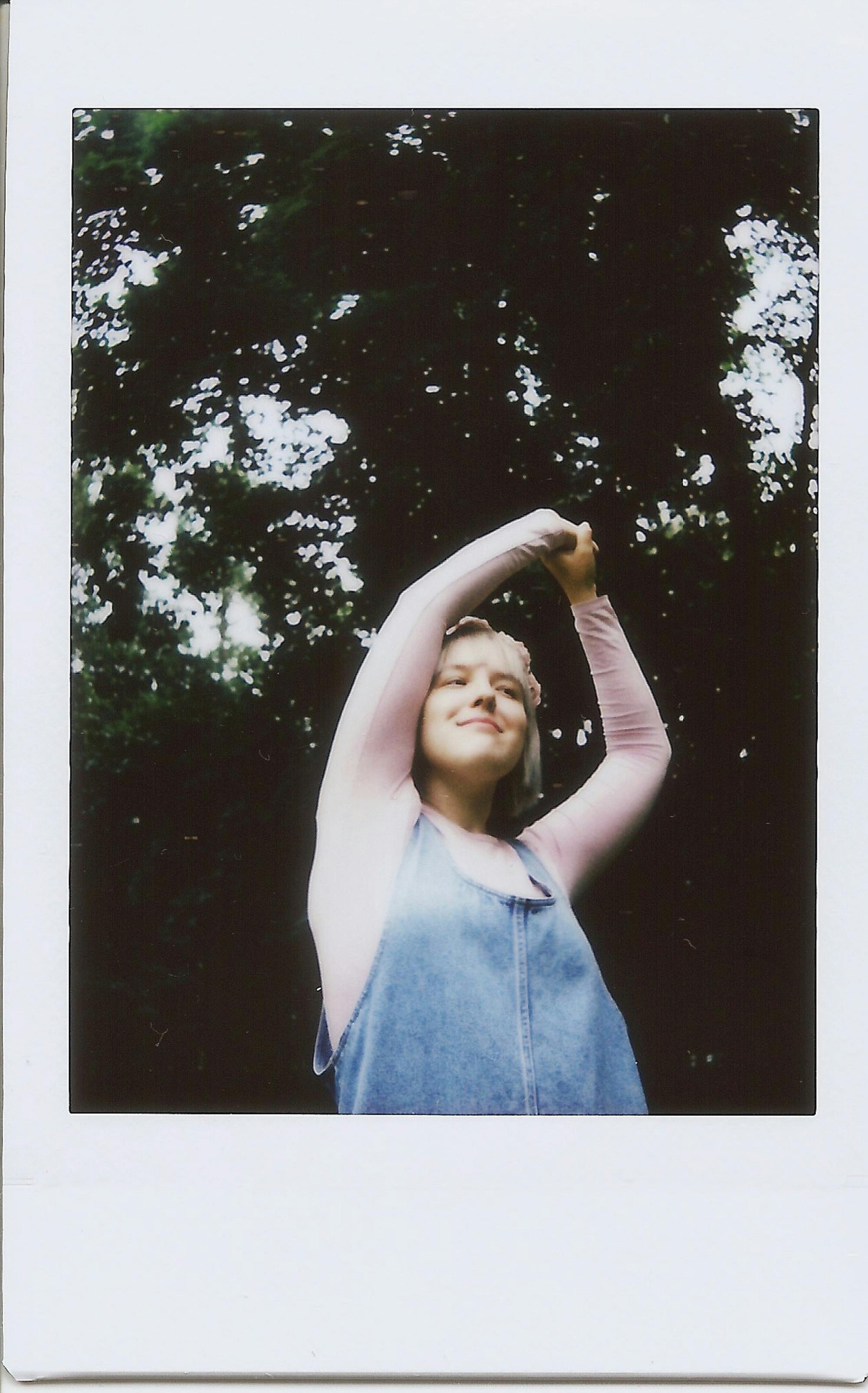Smiling woman with arms raised outdoors, embracing nature and summertime joy.