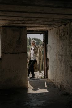一名穿着风衣的男子站在一栋光线昏暗的废弃建筑门口，营造出一种喜怒无常的气氛