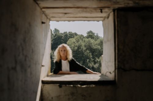 Free Artistic portrait of a woman framed by an abandoned building window, with blurred focus. Stock Photo